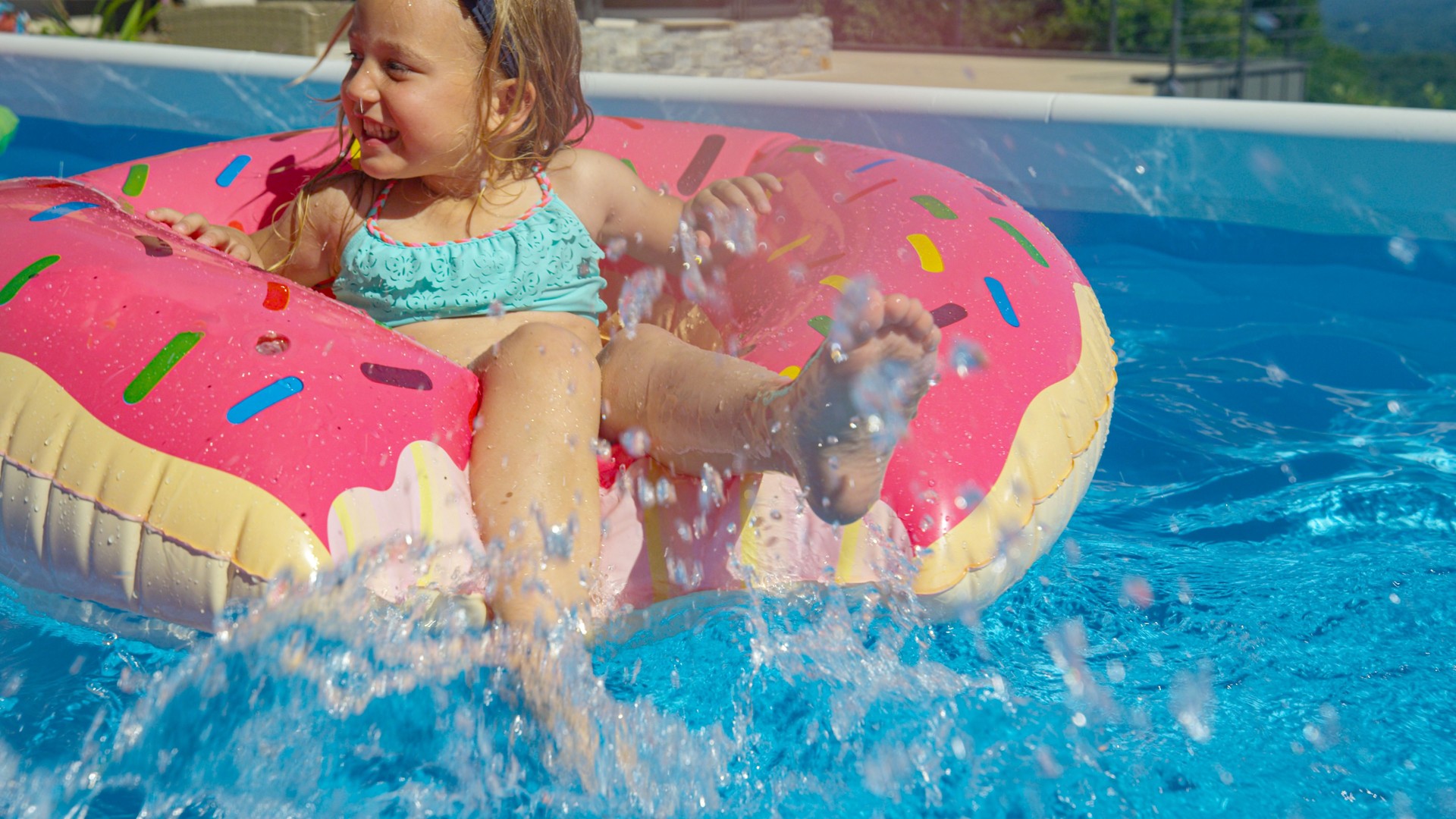CLOSE UP: Adorable girl floating in pool on inflatable donut and splashing water
